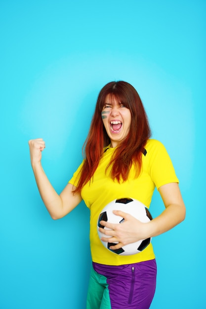 Mulher é fã de futebol com uma camiseta amarela e uma bola de futebol no fundo azul