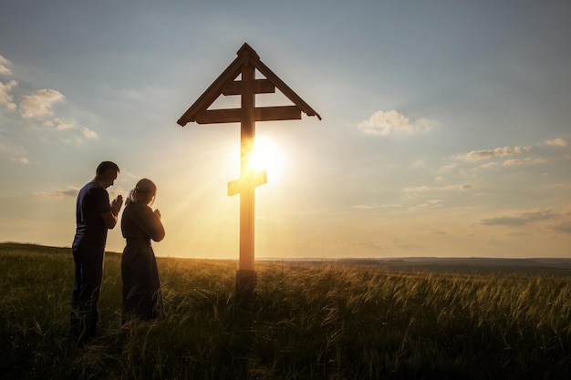 Foto mulher e homem rezando ao ar livre na cruz cristã no fundo do céu pôr do sol