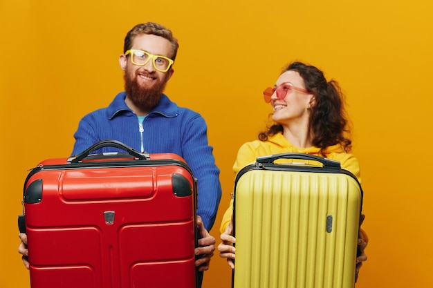 Mulher e homem sorrindo malas na mão com mala amarela e vermelha sorrindo alegremente e fundo amarelo torto indo em uma viagem de férias em família recém-casados