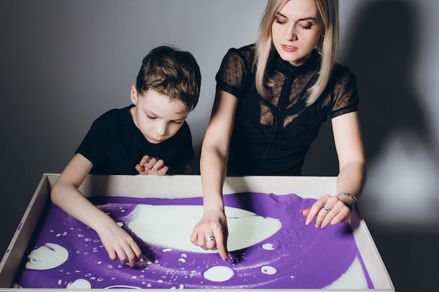 Mulher e menino desenhar em uma mesa de areia interativa