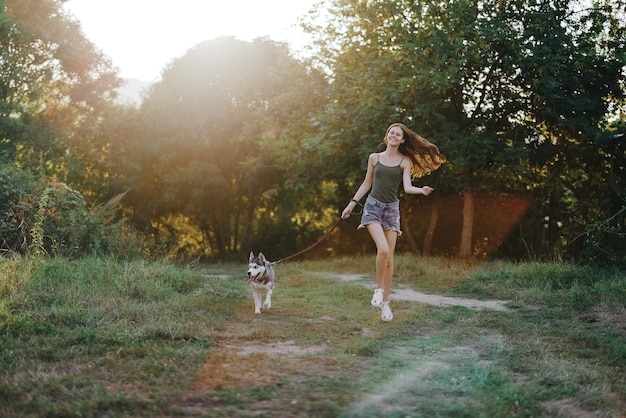 Mulher e seu cachorro husky correndo alegremente pela grama na natureza no parque sorriem com queda de dentes caminham com animal de estimação viajando com um amigo cachorro