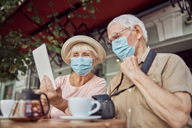 Foto mulher e um homem com máscaras faciais, sentados a uma mesa de madeira em um café