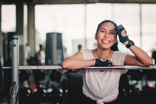 Foto mulher egeia, descansando na mesa de exercício após treino com halteres. conceito: desportiva menina sentada no ginásio.