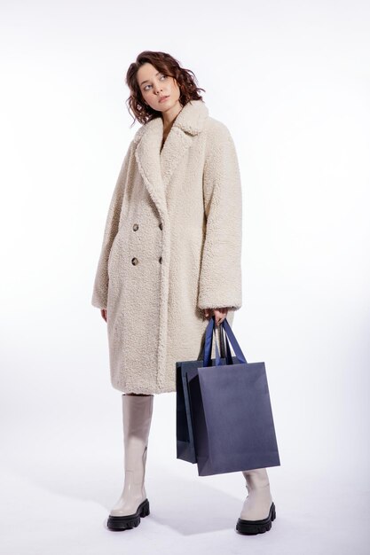 Mulher elegante com casaco de pele bege creme bota duas sacolas de compras azuis posando sobre fundo branco