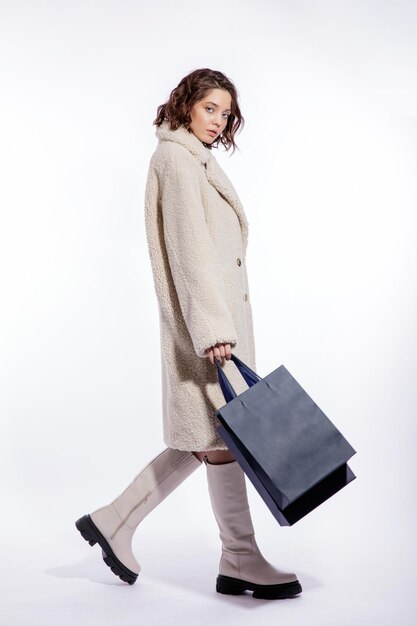 Mulher elegante com casaco de pele bege creme bota duas sacolas de compras azuis posando sobre fundo branco