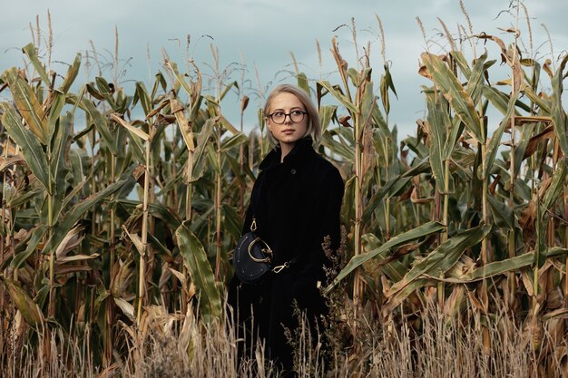 Mulher elegante com casaco preto em campo de milho de outono