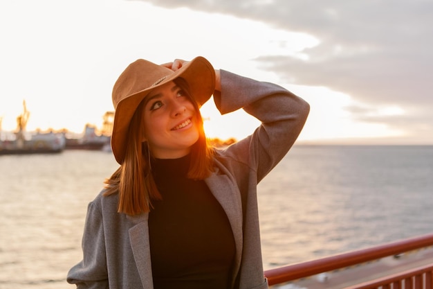 Mulher elegante com chapéu de feltro e casaco ao nascer do sol no mar