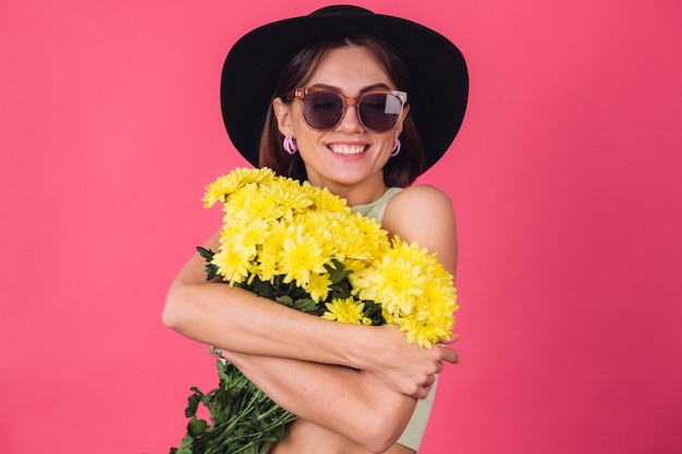 Mulher elegante com chapéu e óculos escuros, abraçando um grande buquê de ásteres amarelos, clima de primavera, calmo e sorridente espaço isolado