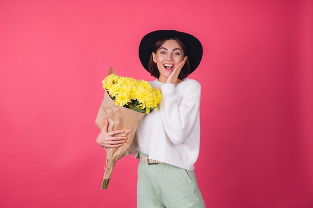 Mulher elegante com chapéu e suéter branco casual na parede vermelha