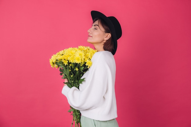 Mulher elegante com chapéu e suéter branco casual na parede vermelha