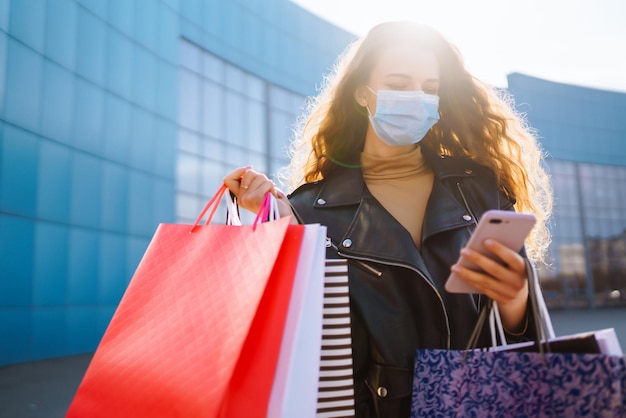 Mulher elegante com máscara médica protetora com sacola de compras usando seu telefone Estilo de moda Blackfriday