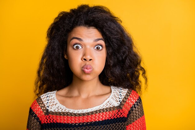 Mulher elegante com penteado afro posando contra a parede laranja