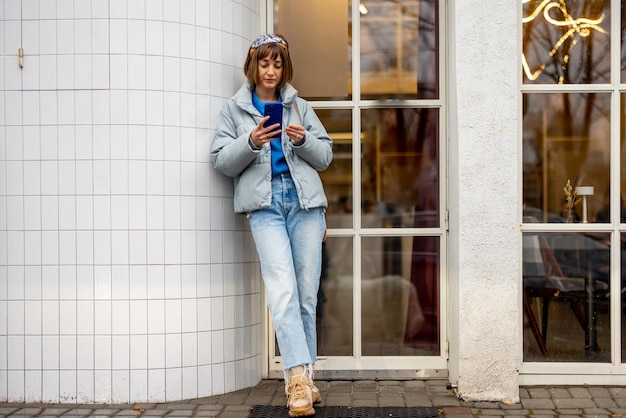 Mulher elegante com telefone perto de café ao ar livre