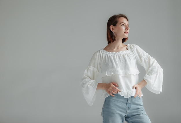 Mulher elegante com uma blusa branca e jeans em um fundo cinzento conceito de graça e feminilidade