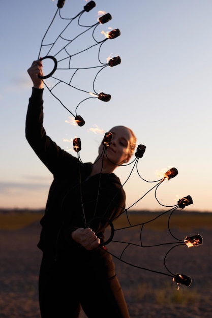 Foto mulher elegante dançando com ventiladores de fogo no céu ao pôr do sol