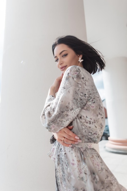 Mulher elegante e elegante em vestido de moda primavera com padrão de flores anda na cidade perto de colunas brancas vintage