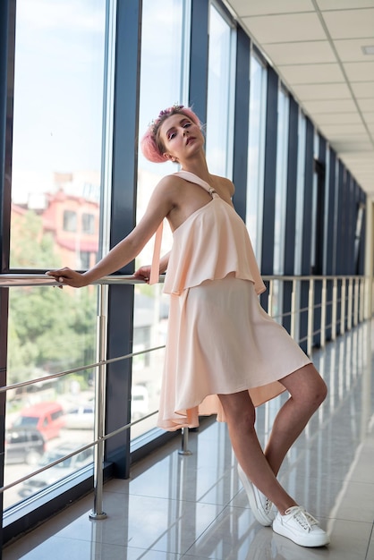 Mulher elegante e jovem de vestido rosa posando dentro de um longo corredor