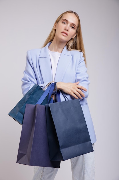 mulher elegante em jeans muito azul, jaqueta em fundo branco, sacolas de compras