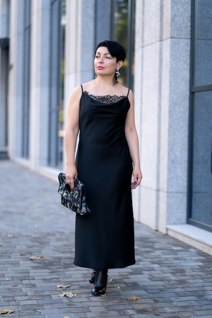 Foto mulher elegante em um elegante vestido preto posando em uma rua da cidade