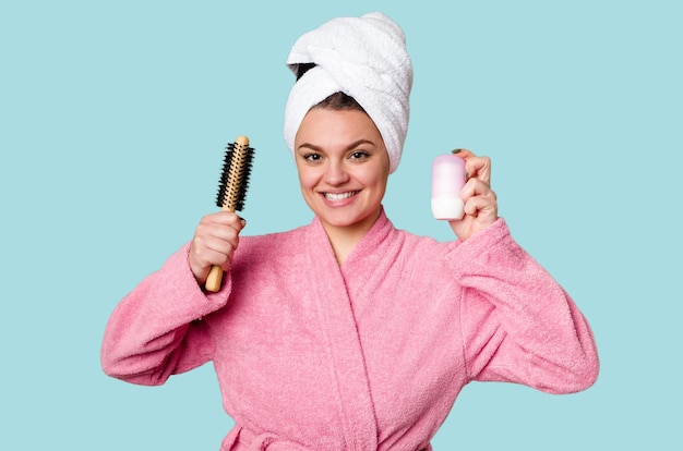 Mulher elegante em um roupão rosa pronto para o dia com uma escova de cabelo e desodorante