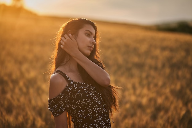 Mulher elegante em um vestido no campo de trigo ao pôr do sol.