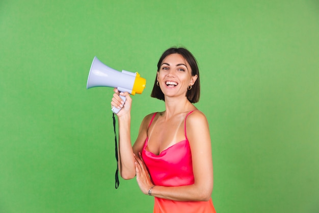 Mulher elegante em vestido de seda rosa em verde, feliz animada alegre alegre gritando no megafone, isolado