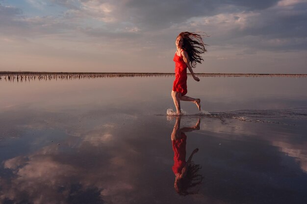 Mulher elegante em vestido de seda vermelho andando por um lago salgado