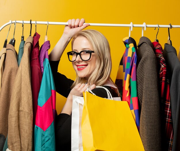 Mulher elegante em vestido formal preto segurando sacolas de compras ao lado de roupas no trilho