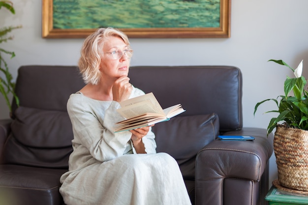 Mulher elegante está lendo um livro enquanto está sentado em um sofá em sua casa.