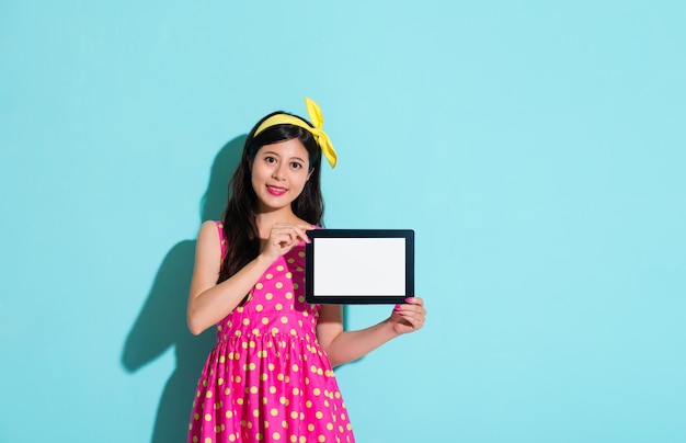 mulher elegante feliz segurando o computador tablet digital móvel mostrando a tela em branco e cara a câmera sorrindo em fundo azul.