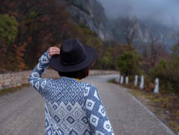 Mulher elegante hipster em um chapéu andando por uma estrada de montanha