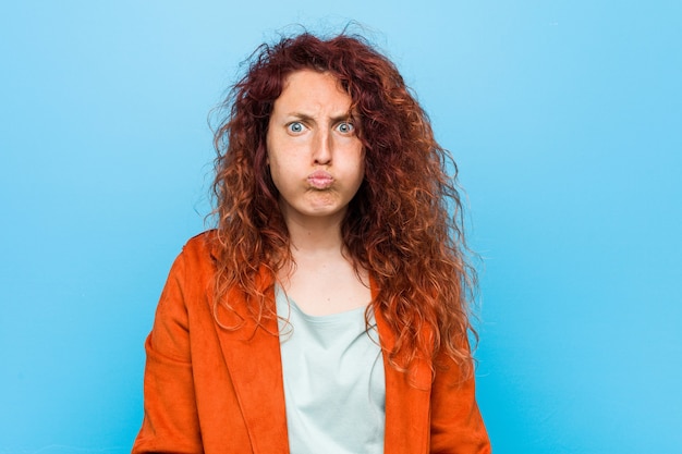 Mulher elegante jovem ruiva assoa as bochechas, tem expressão cansada. Conceito de expressão facial.