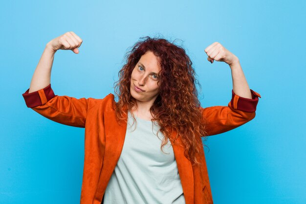 Foto mulher elegante jovem ruiva mostrando gesto de força com os braços, símbolo do poder feminino