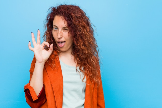 Mulher elegante jovem ruiva pisca um olho e mantém um gesto bem com a mão