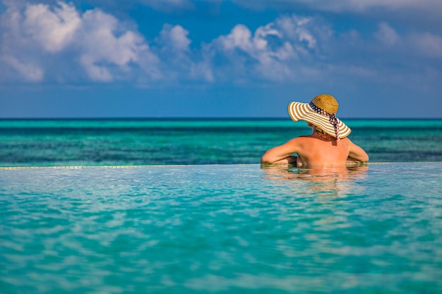 Mulher elegante modelo de biquíni preto, chapéu de palha, resort de luxo de horizonte de mar de piscina infinita, lazer
