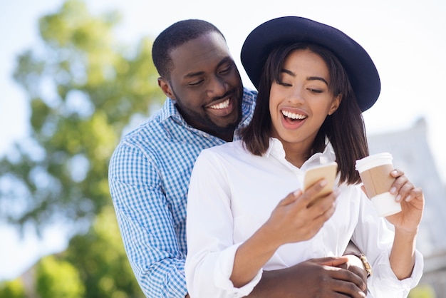 Mulher elegante, moderna e elegante usando seu smartphone para compartilhar coisas interessantes com seu homem enquanto eles estão namorando