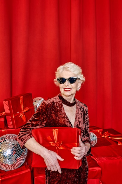 Mulher elegante sênior com presentes em fundo vermelho. festa, moda, celebração, conceito anti-idade