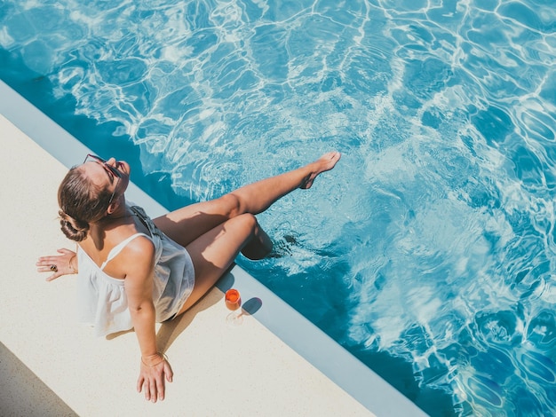 Mulher elegante sentada à beira da piscina no deck vazio