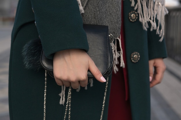 Mulher elegante vestida com casaco verde, posando com bolsa de couro preta na rua. Foto de close