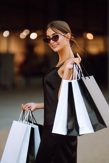 Mulher elegante vestida com um vestido preto com sacolas de compras.