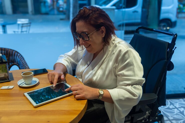 Foto mulher em cadeira de rodas interagindo com tablet ao tomar café