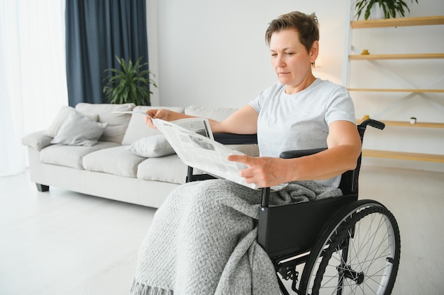 Mulher em cadeira de rodas lendo jornal dentro de casa