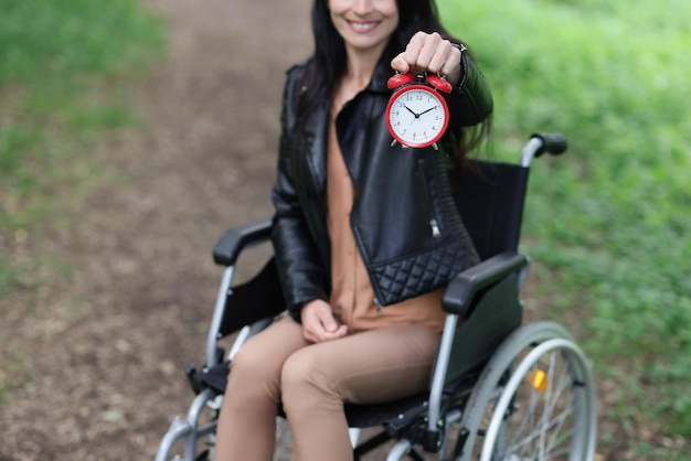 Mulher em cadeira de rodas segura despertador vermelho no parque caminhando e reabilitação para deficientes