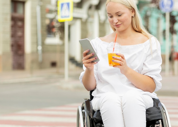 Mulher em cadeira de rodas tomando uma bebida e usando o smartphone com espaço de cópia