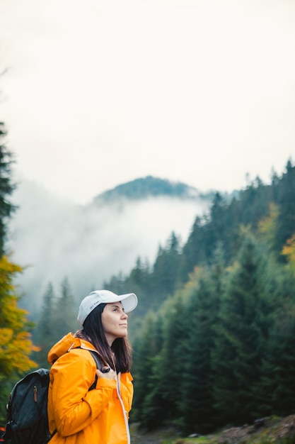 Mulher em caminhante de capa de chuva amarela nas montanhas de outono