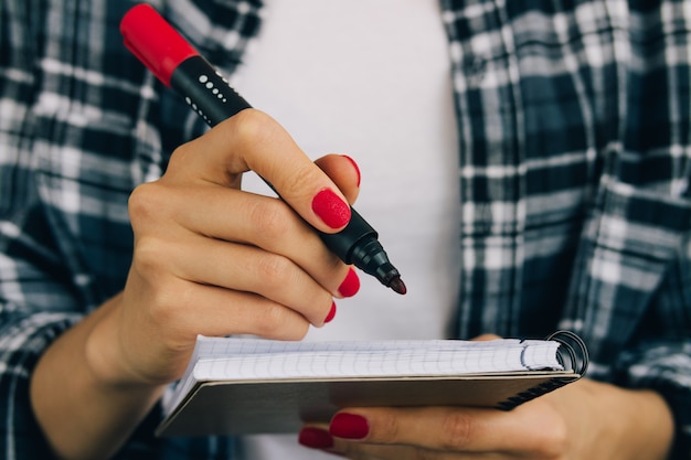 Mulher, em, camisa xadrez, e, manicure vermelho, caneta, escrita, em, um, caderno