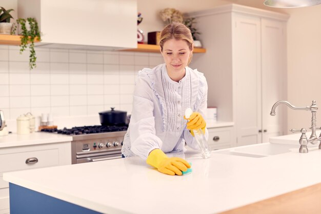 Mulher em casa na cozinha fazendo tarefas domésticas e limpando a superfície do balcão com spray