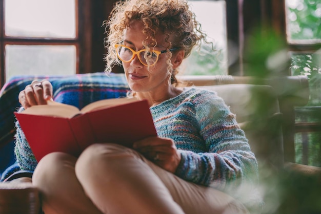Foto mulher em casa sentada e lendo um livro relaxando atividade de lazer em casa pessoas do sexo feminino serenas estudando e lendo romance usando óculos estilo de vida de solteira domingo e férias