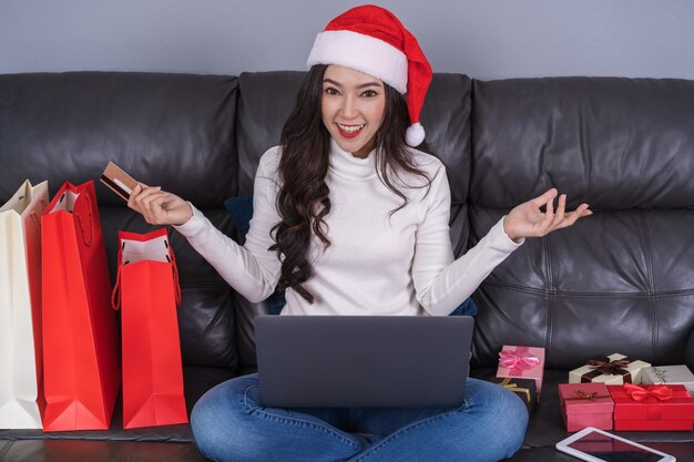 Foto mulher, em, chapéu santa, comprando online, para, presente natal, com, laptop, em, a, sala de estar