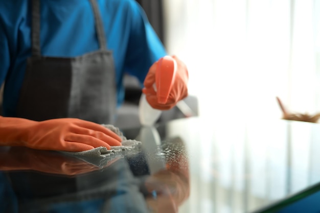 Foto mulher em close-up com luvas de borracha limpando a superfície da mesa de café com um pano de microfibra